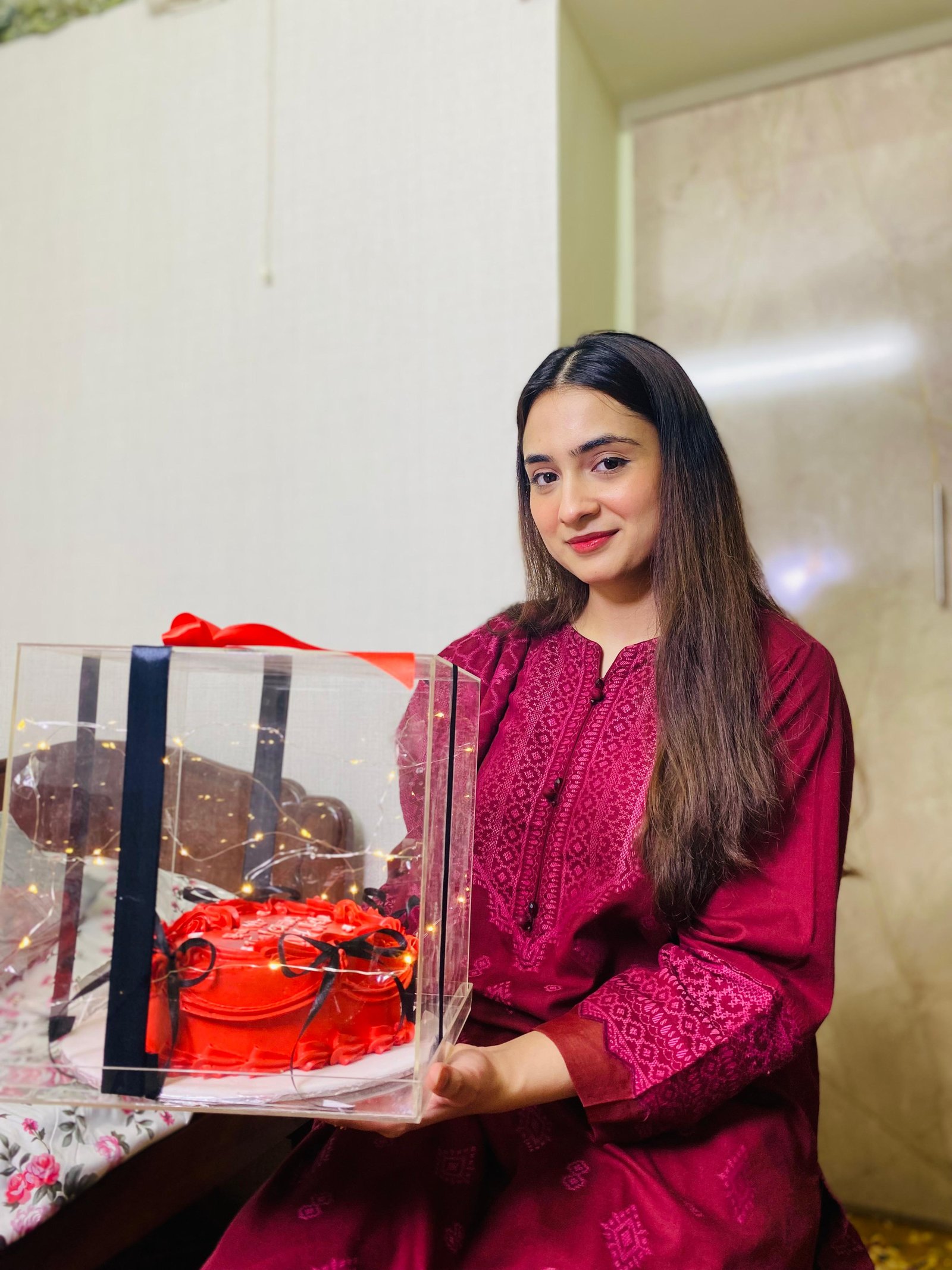 Ayesha beside a cake with a red ribbon
