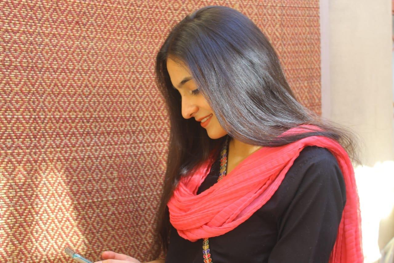 Ayesha with a pink scarf, looking down and smiling